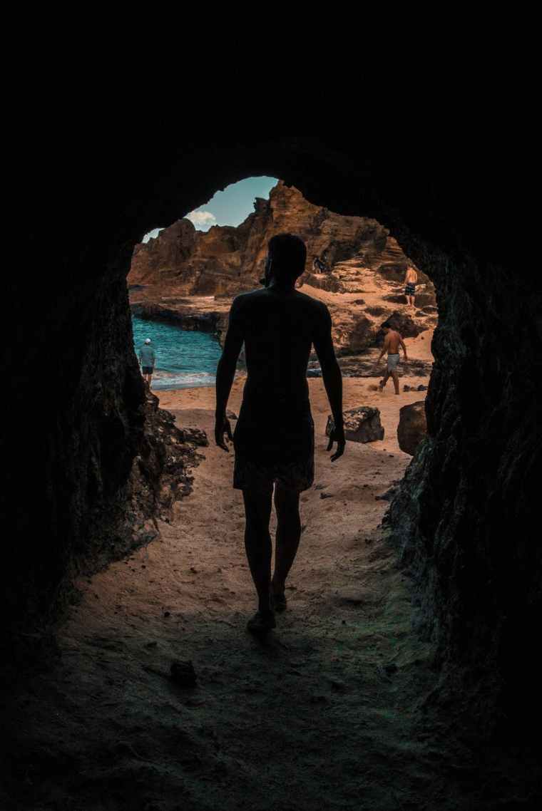 back view photo of person walking out of a cave